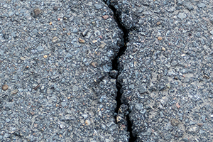 Eine Nahaufnahme von rissigem Asphalt zeigt einen markanten dunklen Riss, der sich durch den rauen, strukturierten Belag zieht - ein idealer Kandidat für die Rissesanierung.